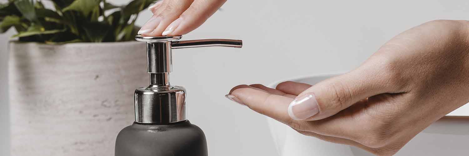 Mujer poniendo jabón en sus manos con la ayuda de un dispensador d jabón.